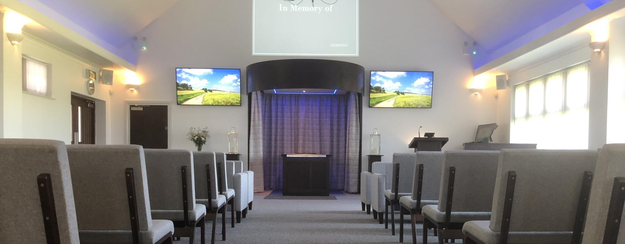 Inside the chapel at Memoria Doncaster, with rows of seating, tribute screens and blue lighting around the curtained committal area